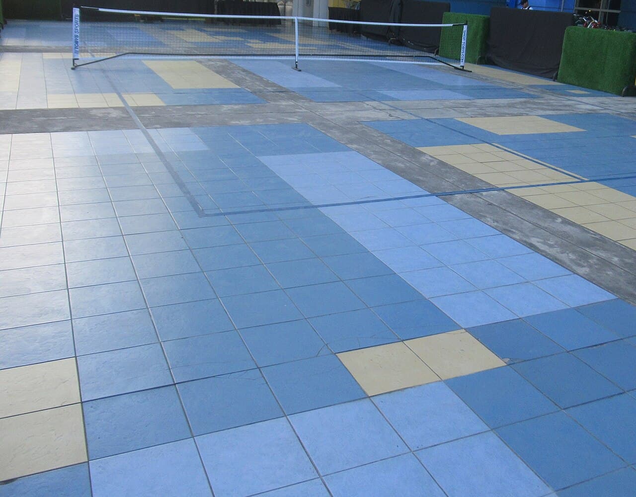 Portable pickleball net on a temporary court marked with tape on an outdoor tiled plaza